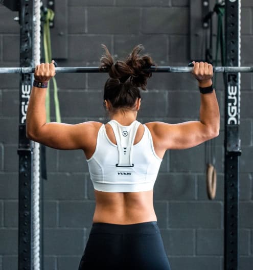 Femeie care face exerciții de forță cu barbell în sala de fitness.